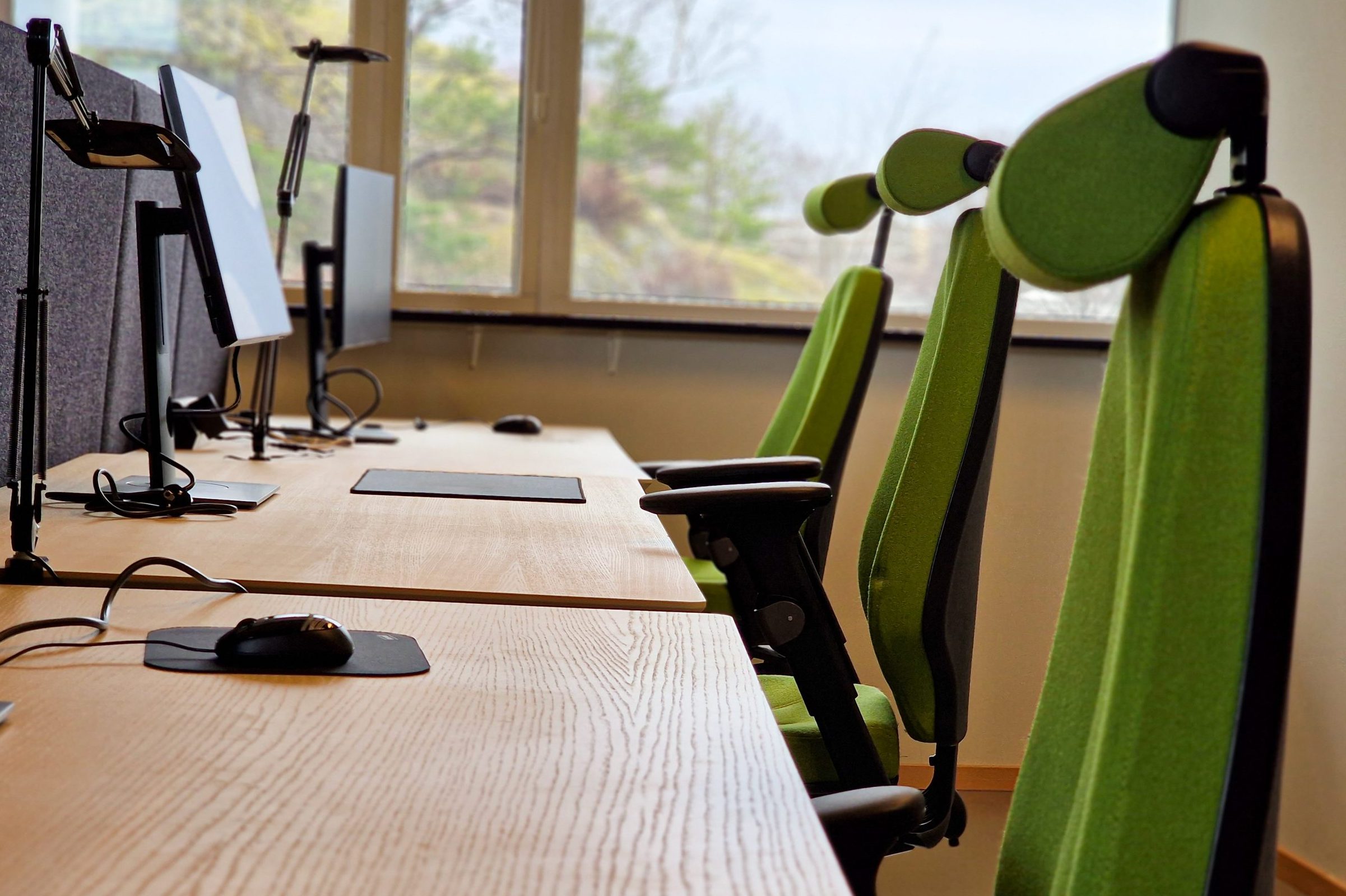 Bild på tre gröna arbetsstolar med skrivbord samt skärm hos Innovation Station Flemingsberg.